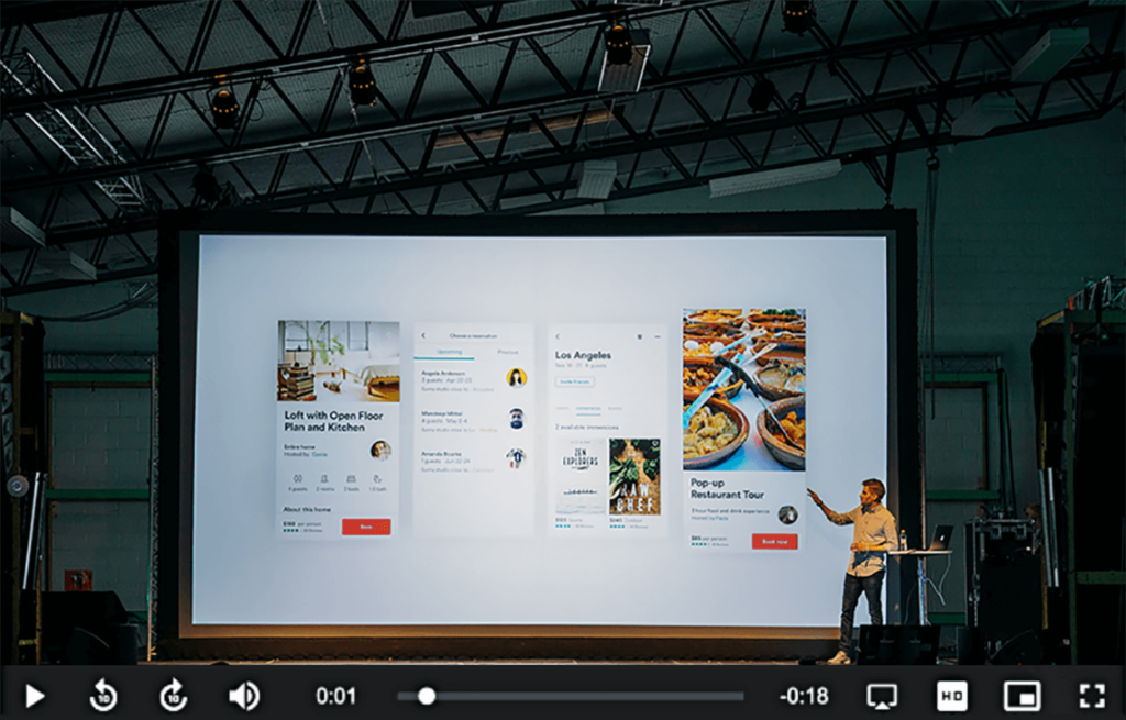 Spreker op een podium naast een groot scherm met videoplayer, video voor betrokkenheid