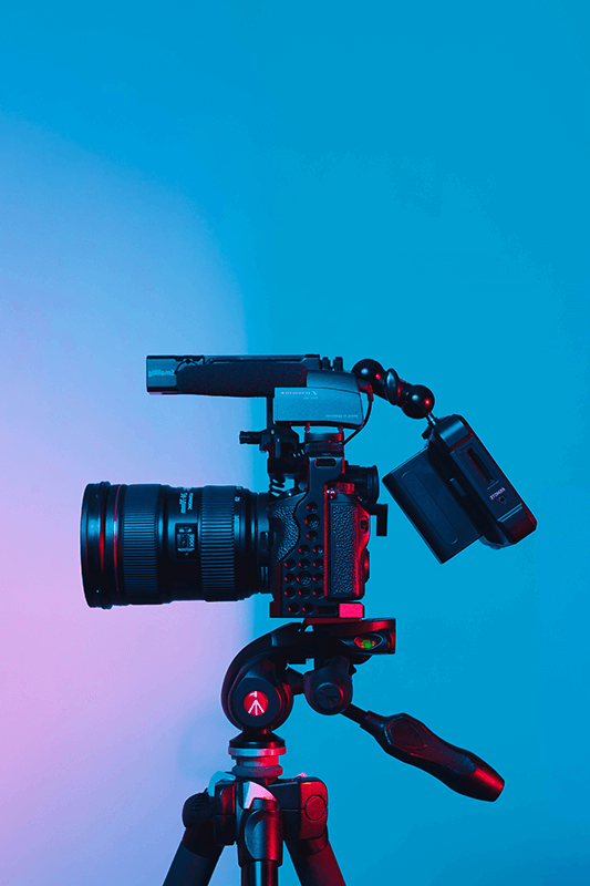 Videocamera op een statief tegen een blauwe achtergrond, als illustratie van het aanleveren van livestreams vanuit studio's